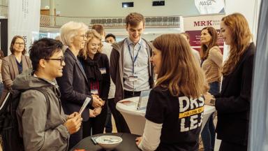 Eine Gruppe von Menschen unterhält sich an einem Messestand