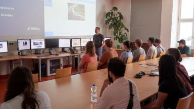 Studierende sitzen in einem Raum und schauen auf eine Präsentation