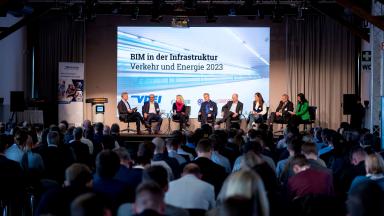 A panel discussion on a stage with 8 participants in front of many spectators