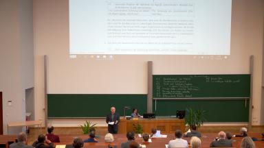 A lecture hall with people sitting at intervals.