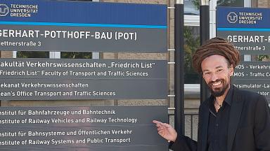 Two men stand to the left and right of a notice board.