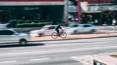  A man is cycling fast in a big city. Around him are cars.