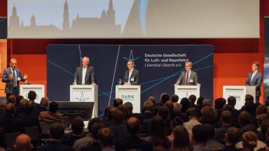 Panel discussion with 5 men in front of a large audience.
