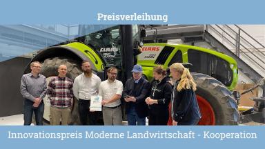 5 men and 2 women stand in front of a tractor. One man is holding a prize, another a certificate.