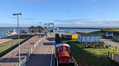 In the foreground is a railway, in the back a station and the North Sea