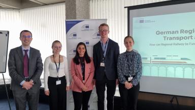 Vier Studierenden mit Betreuer der EIB stehen vor ihrer Präsentation