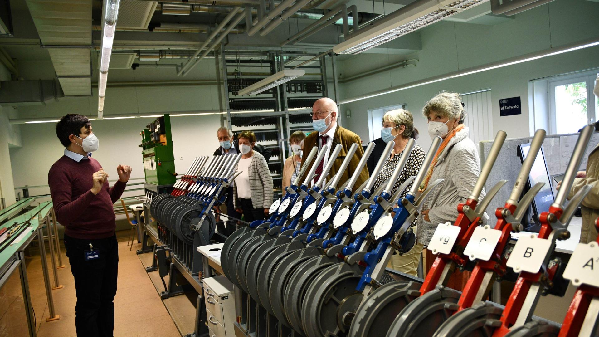 People in a railway laboratory. In the foreground, control levers.
