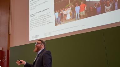 A man gives a lecture in a lecture hall in front of a blackboard