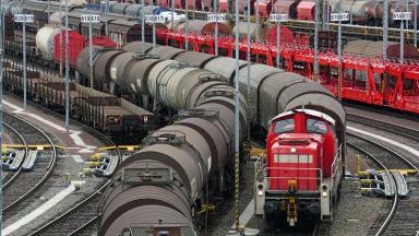 A marshalling yard with many trains with wagons. A locomotive is pulling a train.