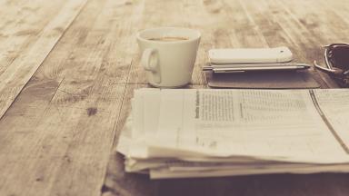 a newspaper lies on the table, next to it a cup of coffee.