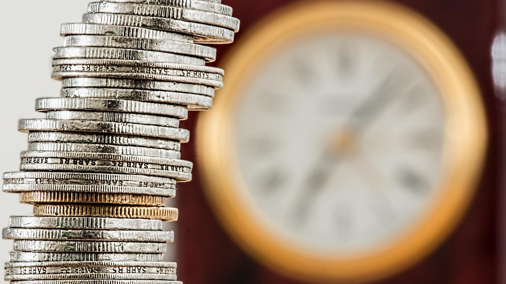 A tower of money coins and a clock in the background