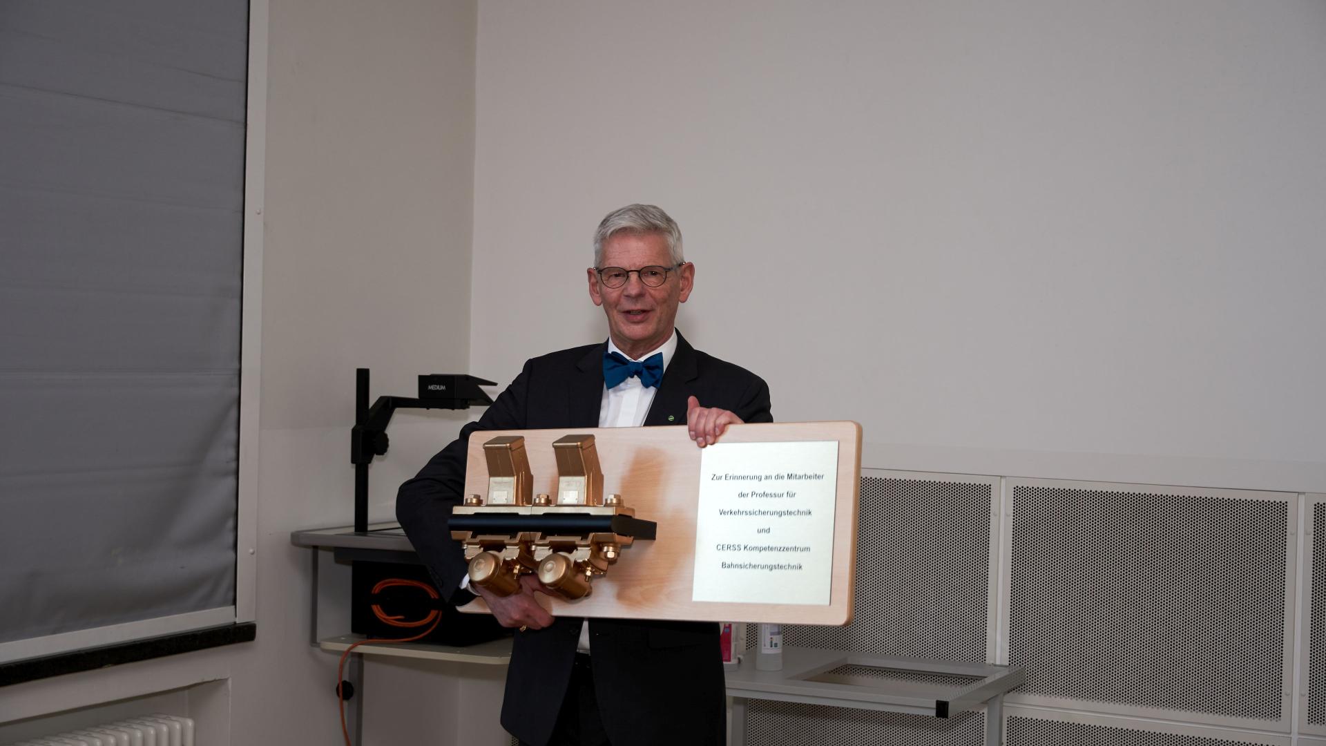 Ein älterer Mann mit Fliege hält ein Geschenk