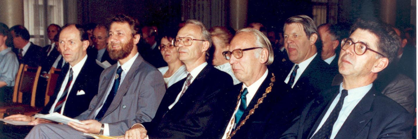 Männer in Anzügen sitzen in einer Reihe.