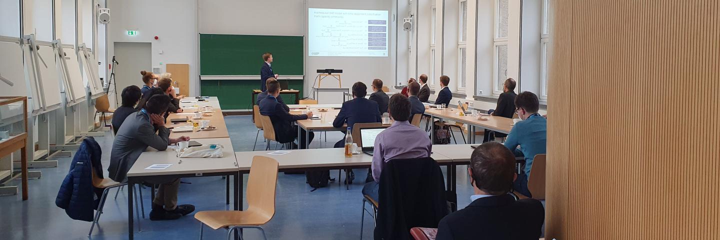 Ein Seminarraum mit Menschen. Einer hält vorn einen Vortrag.