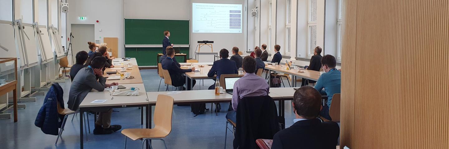 A seminar room with people. One of them is giving a lecture at the front.