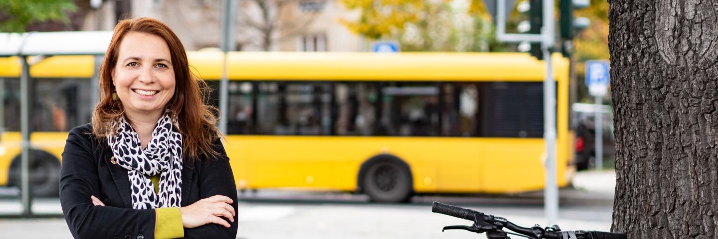 A woman stands in front of a tram with her arms crossed