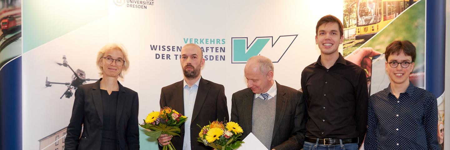 People standing in front of a screen, on the left a woman and then 5 men