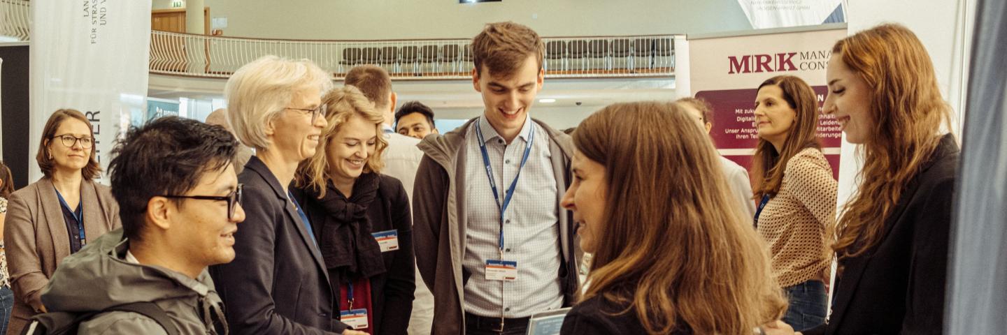 Eine Gruppe von Menschen unterhält sich an einem Messestand