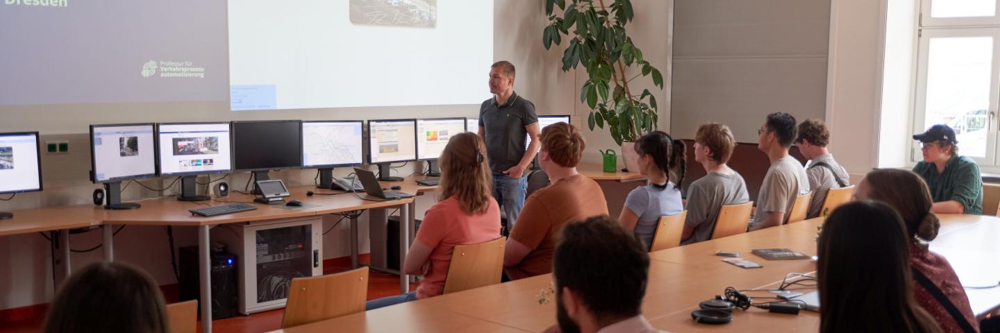 Studierende sitzen in einem Raum und schauen auf eine Präsentation