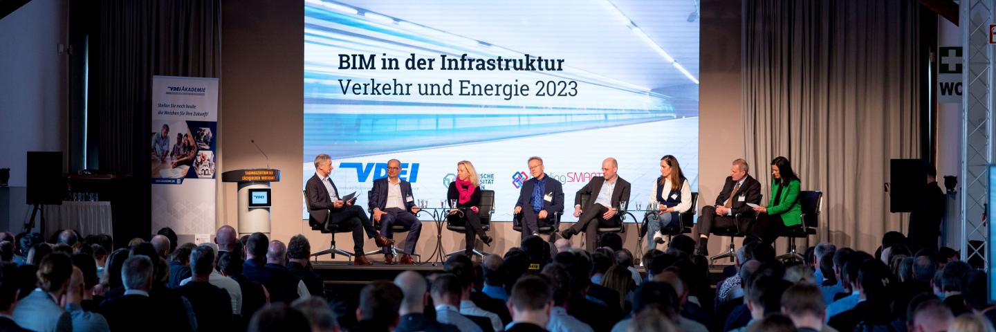 Ein Podiumsgespräch auf einer Bühne mit 8 Teilnehmenden vor vielen Zuschauern