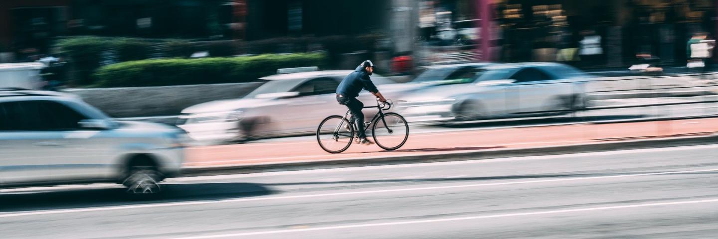  A man is cycling fast in a big city. Around him are cars.
