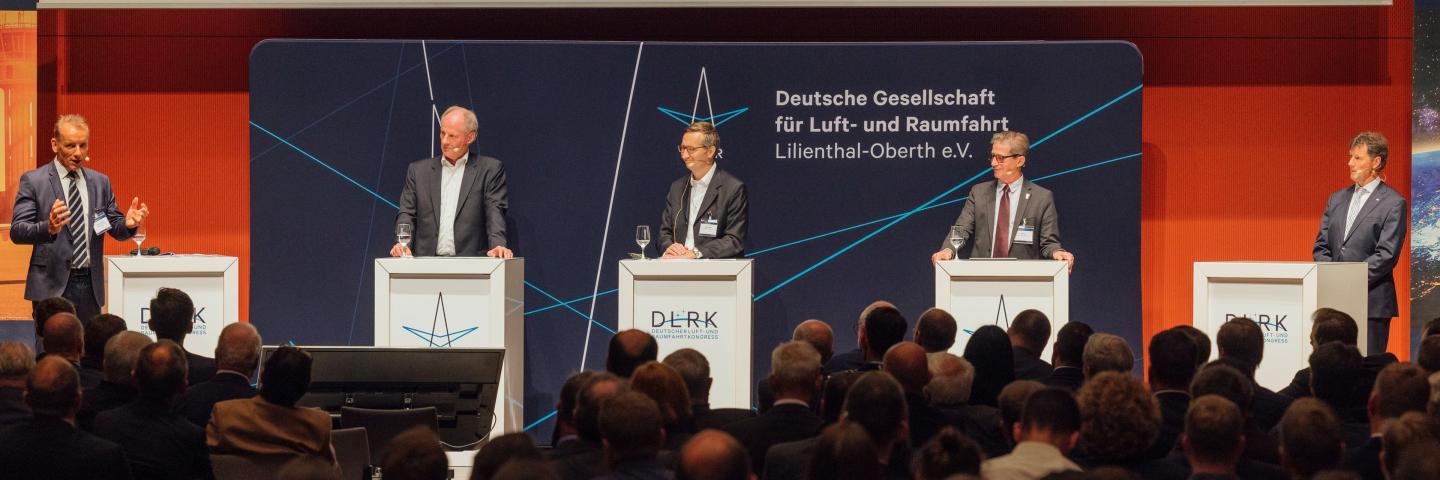 Panel discussion with 5 men in front of a large audience.