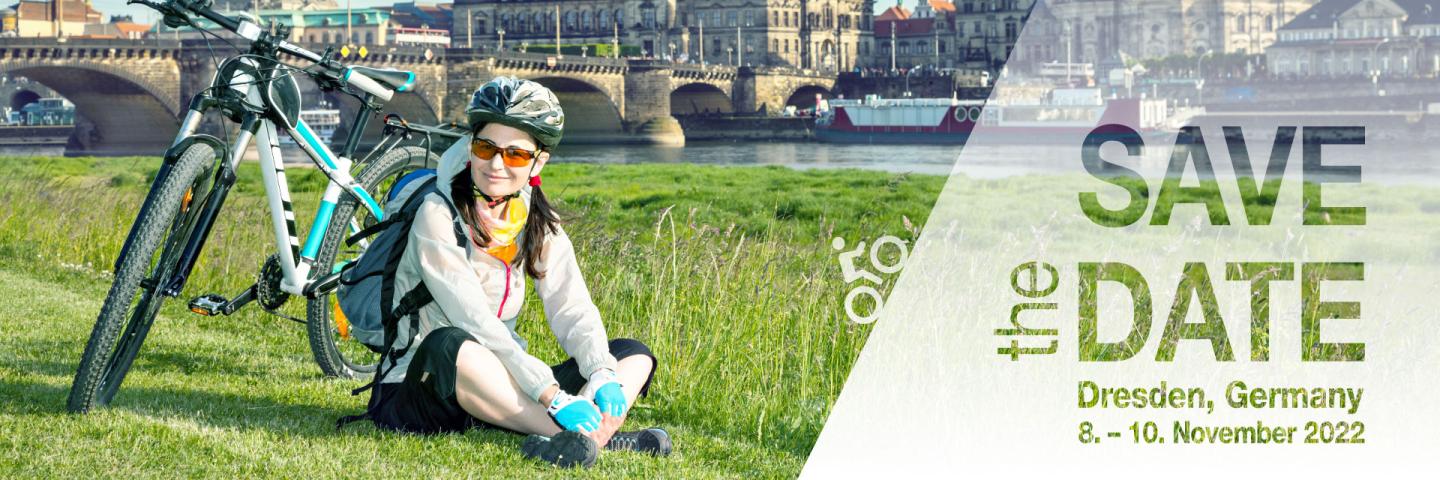 A cyclist sits on a meadow, her bike next to her, the old town of Dresden in the background.