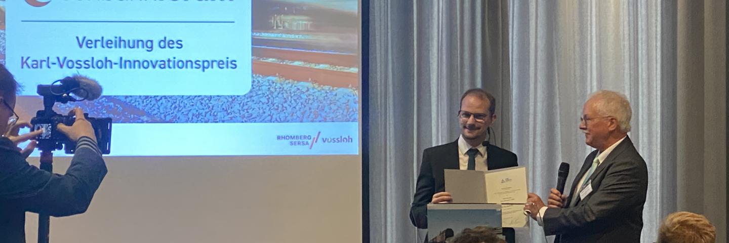 2 Männer auf einem Podium mit Preisübergabe