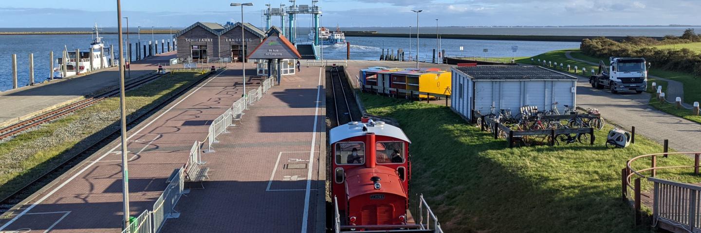 In the foreground is a railway, in the back a station and the North Sea