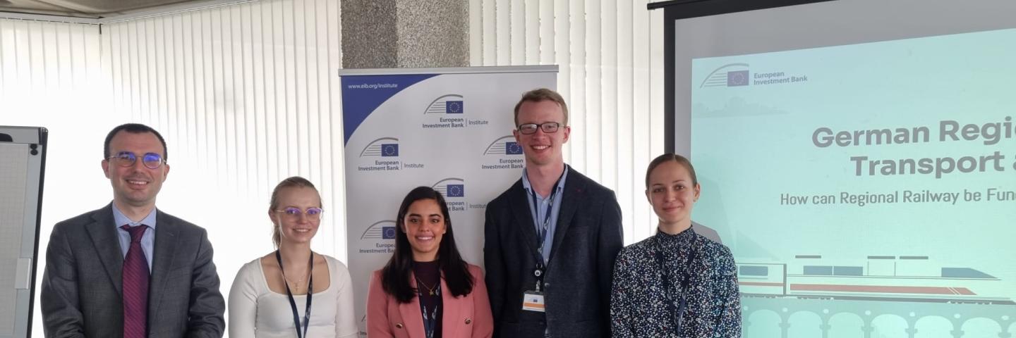 Vier Studierenden mit Betreuer der EIB stehen vor ihrer Präsentation