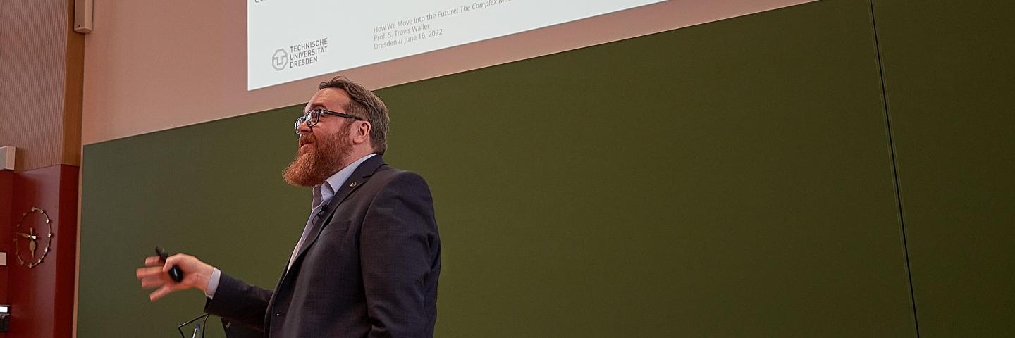 A man gives a lecture in a lecture hall in front of a blackboard