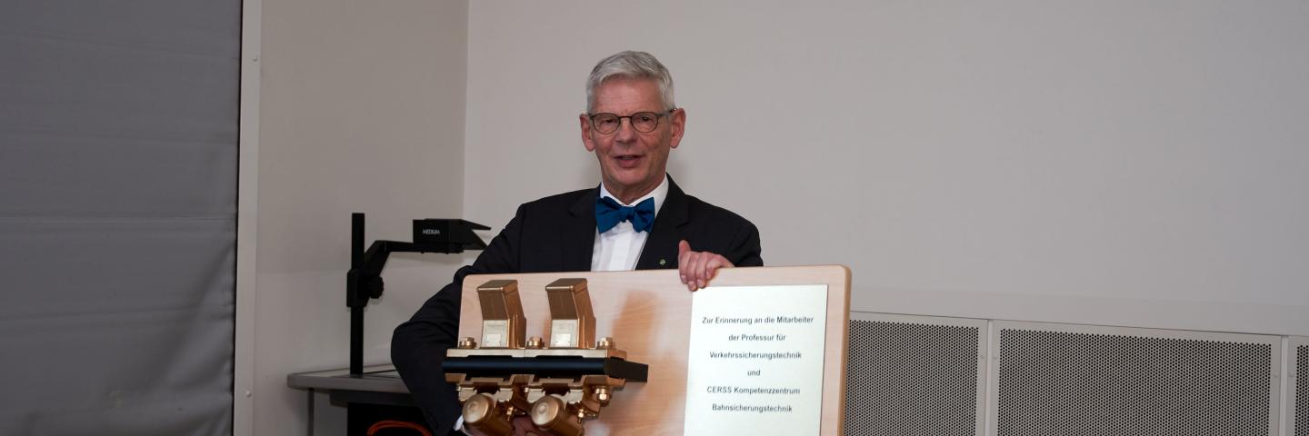 Ein älterer Mann mit Fliege hält ein Geschenk