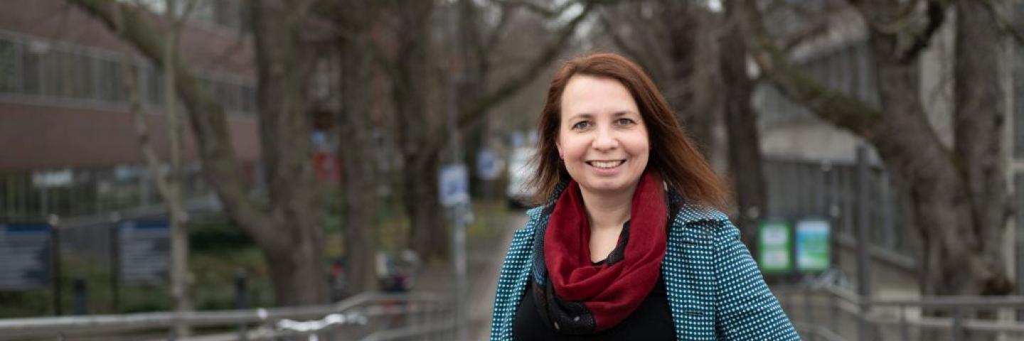 Porträtfoto von Angela Francke im Mantel und mit Hand in die Seite gestützt.