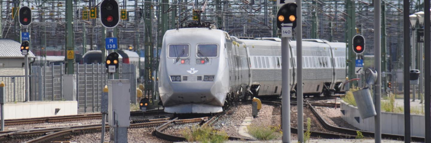 Ein grauer Zug zwischen vielen Gleisen und Oberleitungen